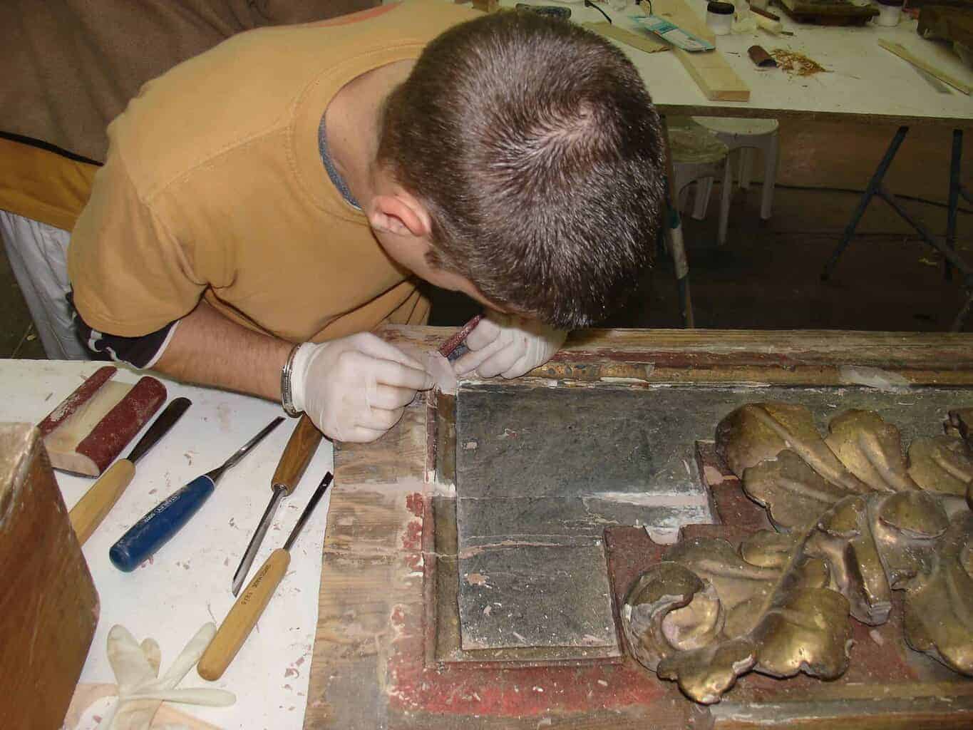 Alumno aplicando técnicas de restauración en madera dorada durante un curso práctico de oficios artísticos impartido por El Barco