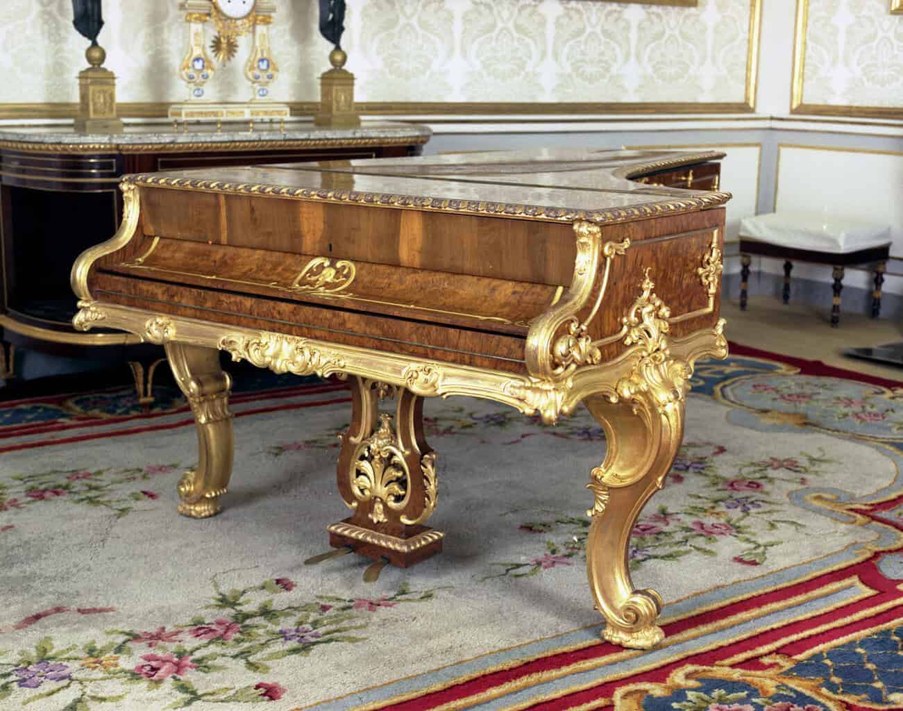 Piano de cola palaciego en maderas nobles con marquetería y patas talladas doradas al agua.