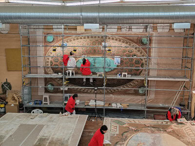 Trabajadores restauran mosaico artístico en taller especializado.